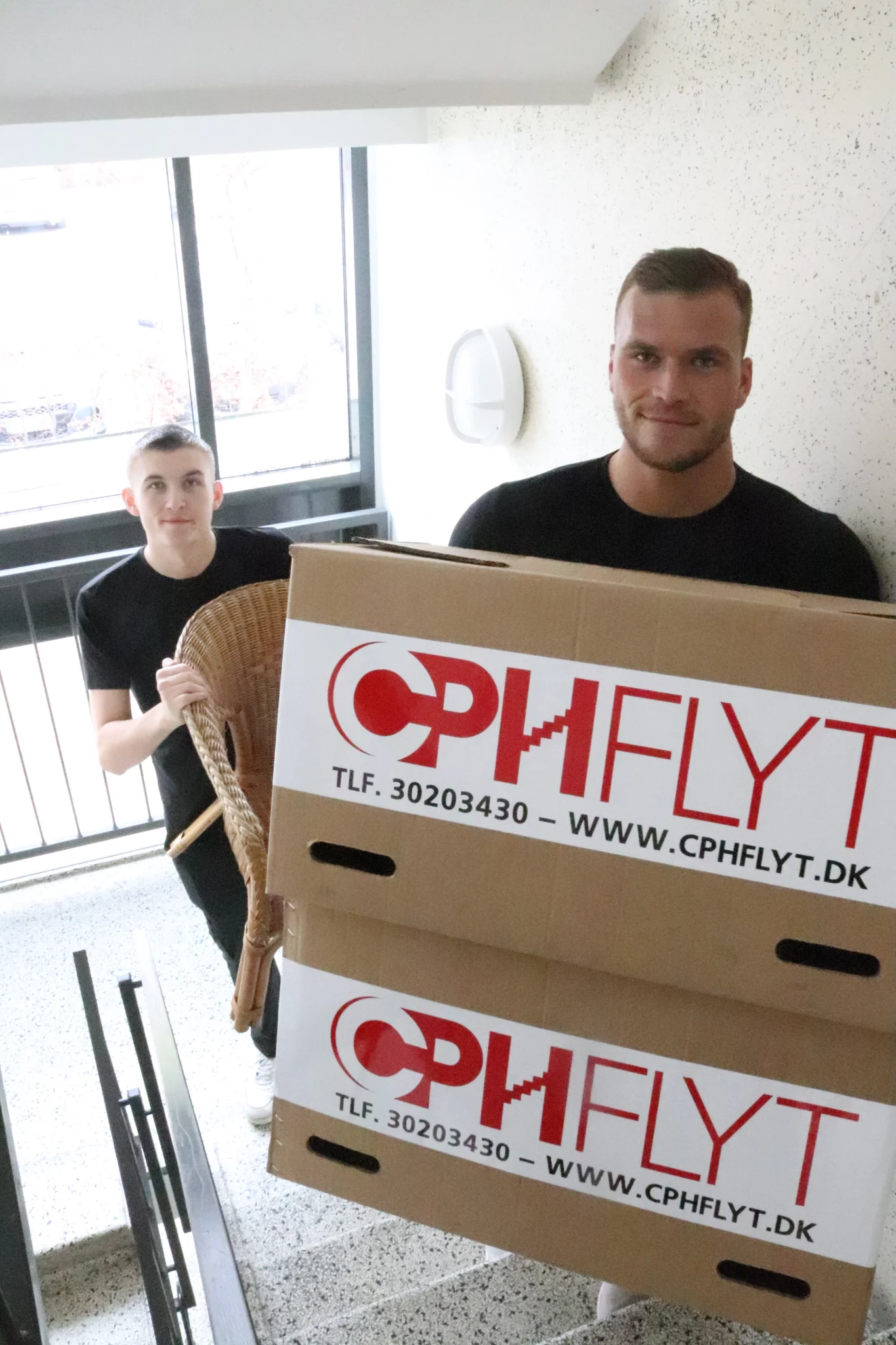 To flyttemænd fra CPHFLYT bærer flyttekasser og et møbel på en trappe